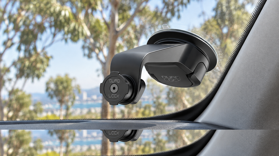 Black Quad Lock QLM-CAR-6 suction mount attached inside a car windscreen, with eucalyptus trees outside.